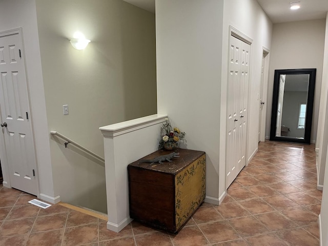 corridor featuring baseboards, visible vents, an upstairs landing, and tile patterned floors