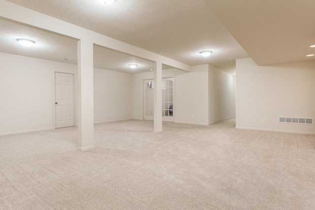 finished basement featuring baseboards, a textured ceiling, visible vents, and light colored carpet