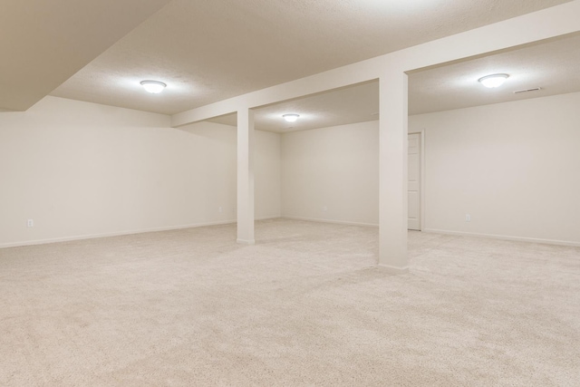 finished below grade area featuring visible vents, light colored carpet, a textured ceiling, and baseboards