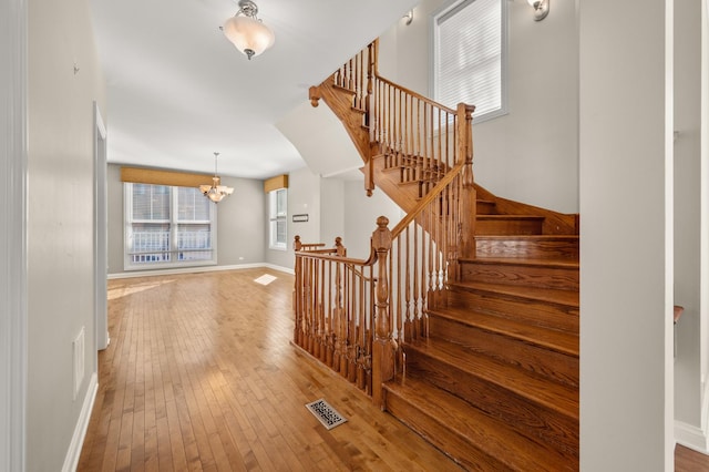 stairway with a chandelier, visible vents, baseboards, and wood finished floors