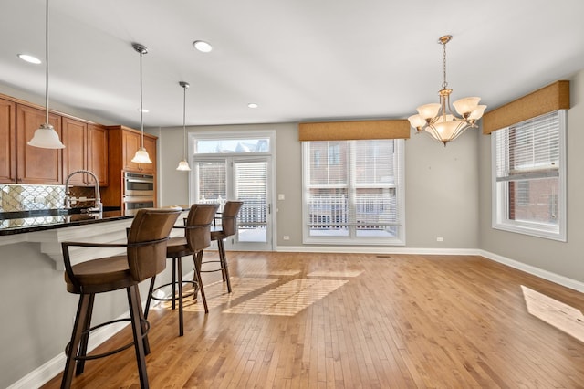 kitchen featuring decorative light fixtures, dark countertops, backsplash, light wood-style floors, and a kitchen bar