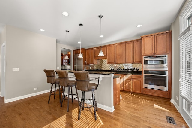 kitchen with stainless steel appliances, dark countertops, visible vents, hanging light fixtures, and brown cabinetry