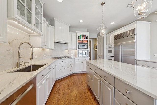 kitchen with a sink, white cabinets, built in appliances, decorative light fixtures, and light wood-type flooring