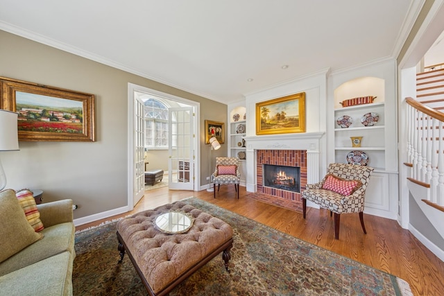 living area featuring wood finished floors, baseboards, a fireplace, ornamental molding, and stairs