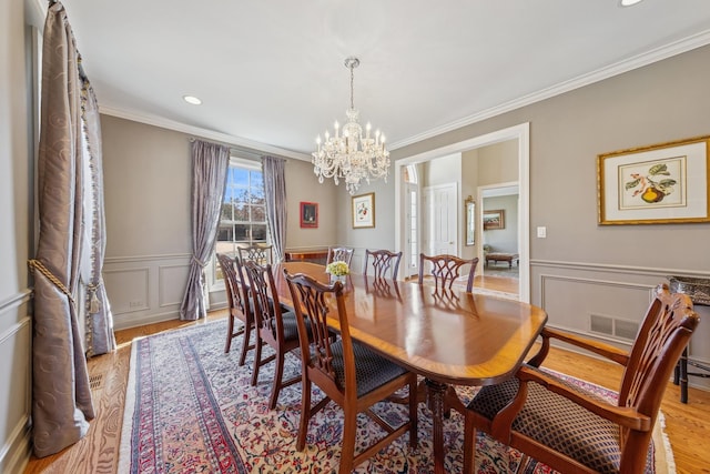 dining room featuring visible vents, crown molding, a chandelier, light wood-type flooring, and wainscoting