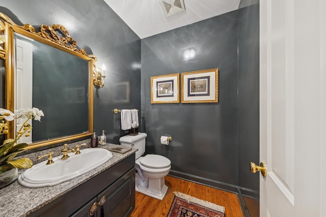 half bath featuring visible vents, baseboards, toilet, wood finished floors, and vanity