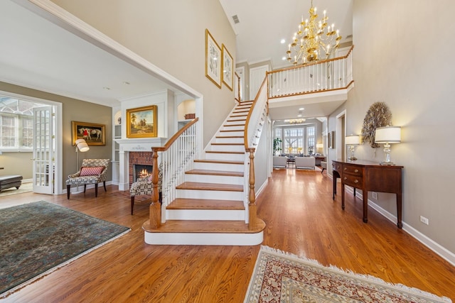 stairs featuring visible vents, a brick fireplace, baseboards, ornamental molding, and wood finished floors