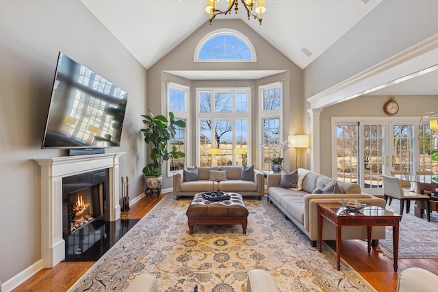 living room featuring visible vents, baseboards, a fireplace with flush hearth, wood finished floors, and high vaulted ceiling