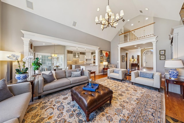 living area featuring decorative columns, high vaulted ceiling, an inviting chandelier, and wood finished floors