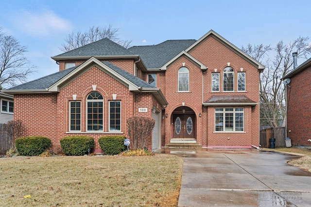 view of front of property with a shingled roof, a front yard, concrete driveway, and brick siding