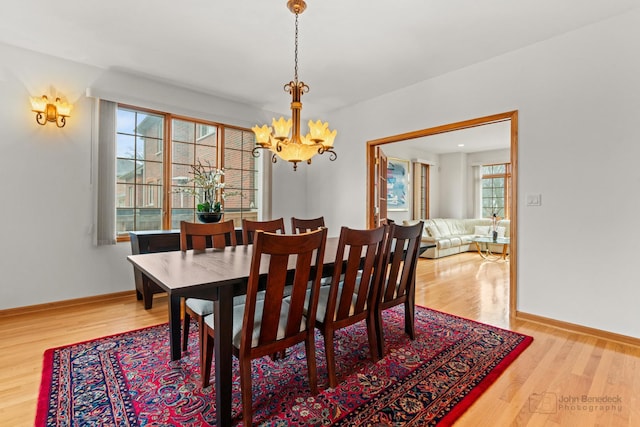 dining area with baseboards, light wood finished floors, and an inviting chandelier