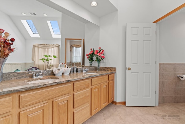 bathroom featuring vaulted ceiling with skylight, tile patterned flooring, visible vents, and a sink