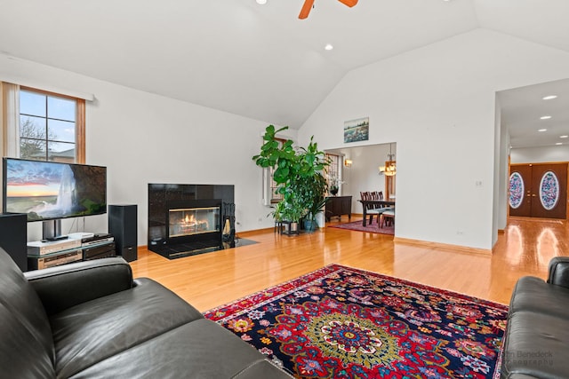 living area featuring ceiling fan, a tile fireplace, wood finished floors, and baseboards