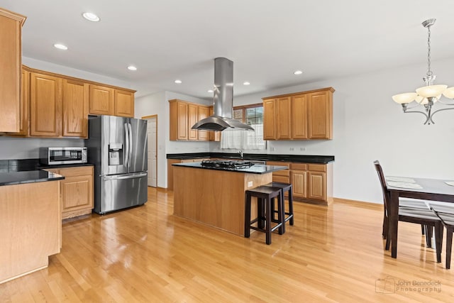 kitchen featuring stainless steel appliances, dark countertops, a kitchen island, island range hood, and light wood-type flooring