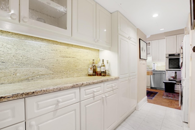 kitchen with white cabinets, light stone counters, stainless steel appliances, and backsplash