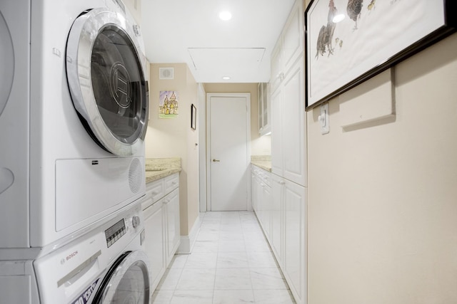 laundry room with marble finish floor, cabinet space, and stacked washer / drying machine