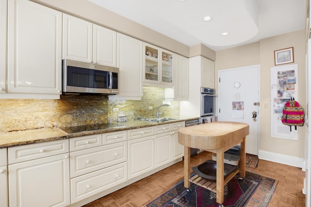 kitchen with appliances with stainless steel finishes, glass insert cabinets, a sink, and white cabinetry