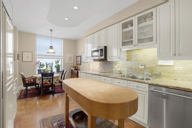 kitchen featuring decorative light fixtures, stainless steel appliances, a sink, white cabinets, and glass insert cabinets