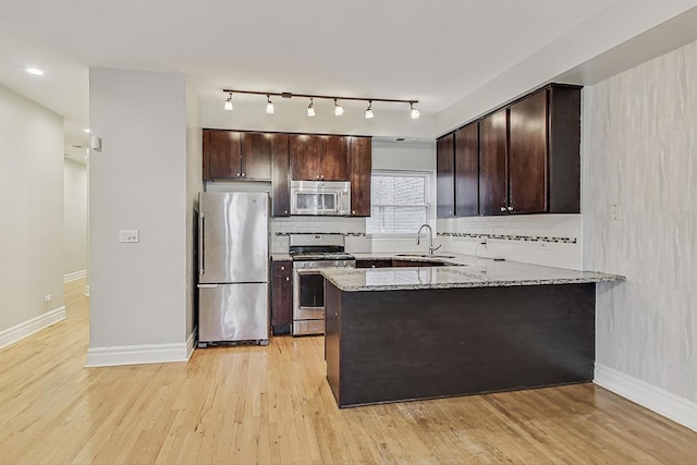 kitchen featuring dark brown cabinetry, a peninsula, stainless steel appliances, light wood-style floors, and a sink