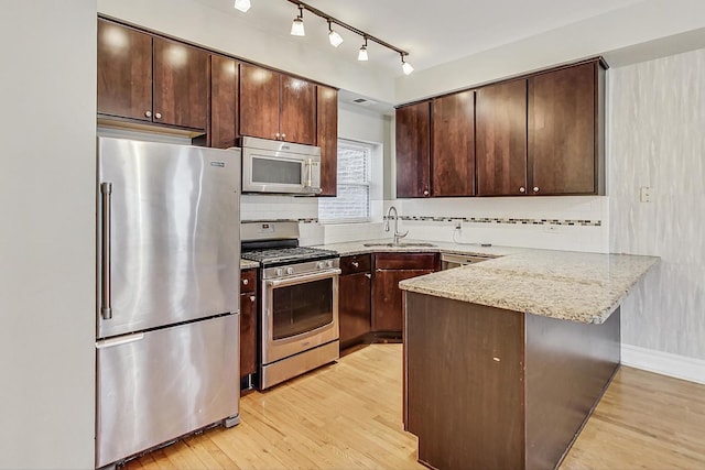 kitchen with light wood finished floors, appliances with stainless steel finishes, a peninsula, dark brown cabinets, and a sink