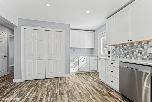 kitchen with white cabinets, light countertops, stainless steel dishwasher, and wood finished floors