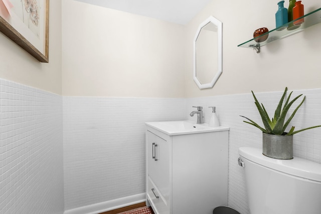 bathroom with wainscoting, vanity, toilet, and tile walls