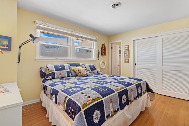 bedroom with a closet, wood finished floors, visible vents, and baseboards