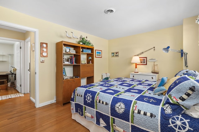 bedroom with baseboards, visible vents, and wood finished floors