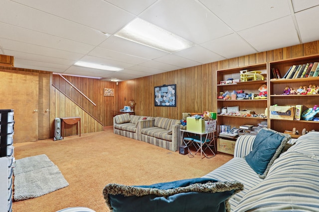 living area with wood walls, carpet, stairs, and a drop ceiling