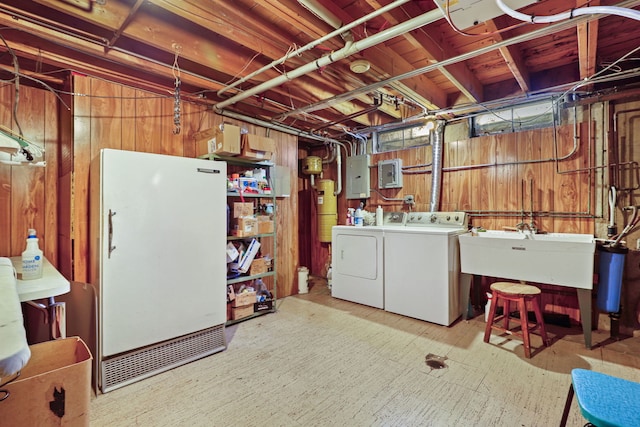 unfinished below grade area featuring wooden walls, electric panel, freestanding refrigerator, separate washer and dryer, and a sink