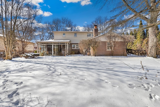 snow covered property with a sunroom, a chimney, and brick siding