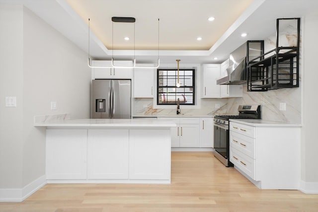 kitchen featuring white cabinets, appliances with stainless steel finishes, a peninsula, wall chimney range hood, and pendant lighting