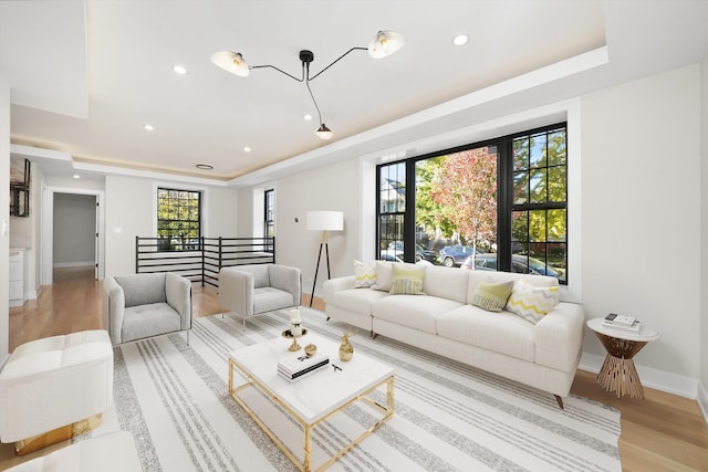 living area featuring a tray ceiling, baseboards, light wood finished floors, and recessed lighting