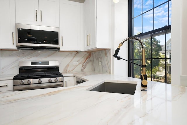 kitchen featuring stainless steel appliances, light stone counters, a sink, and white cabinetry