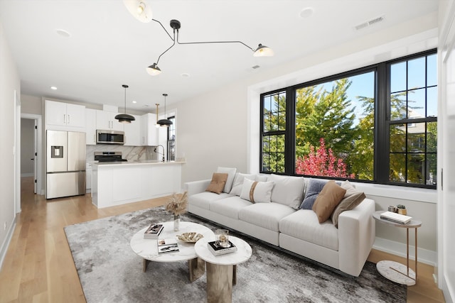 living area with a wealth of natural light, light wood-type flooring, visible vents, and baseboards