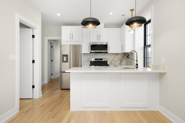 kitchen with a peninsula, a sink, white cabinetry, light countertops, and appliances with stainless steel finishes