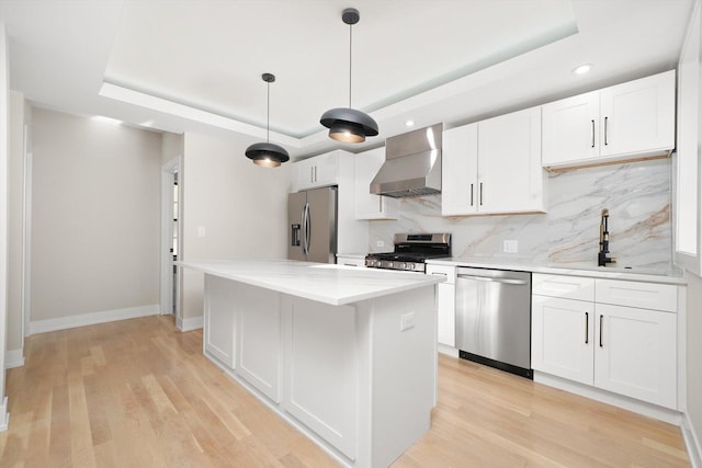 kitchen featuring stainless steel appliances, a sink, white cabinets, wall chimney exhaust hood, and a tray ceiling