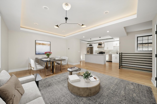 living room featuring a tray ceiling, light wood-style flooring, baseboards, and recessed lighting