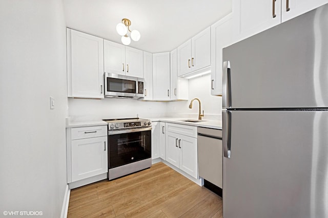 kitchen with light wood-style flooring, stainless steel appliances, light countertops, white cabinetry, and a sink