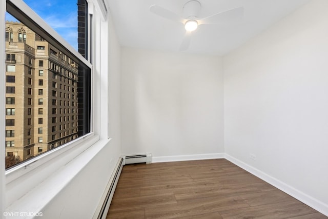 empty room with baseboard heating, ceiling fan, baseboards, and wood finished floors