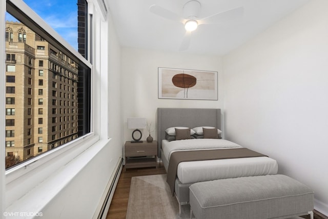 bedroom featuring dark wood-style floors, a baseboard heating unit, a ceiling fan, and baseboards