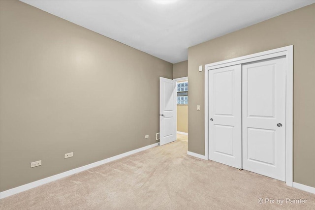 unfurnished bedroom featuring baseboards, a closet, and light colored carpet