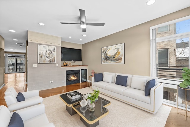 living room with ceiling fan, a lit fireplace, wood finished floors, and recessed lighting