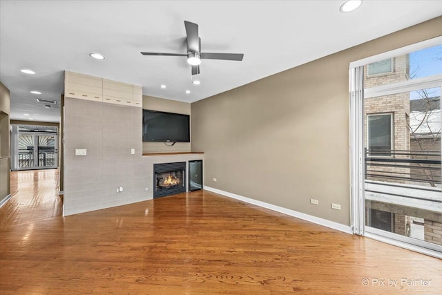 unfurnished living room with a lit fireplace, recessed lighting, dark wood finished floors, and baseboards