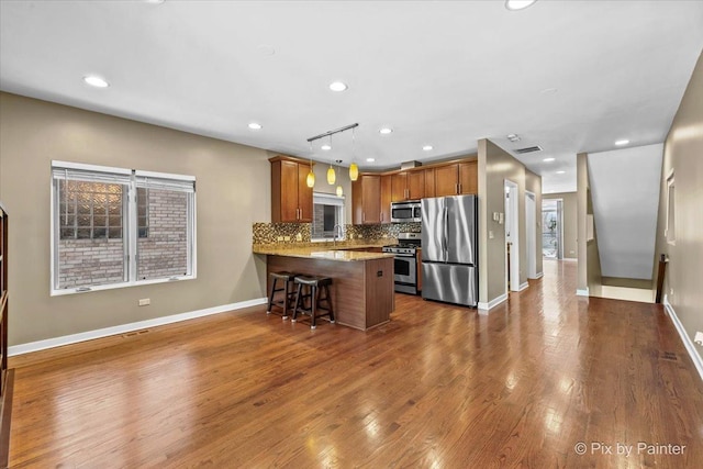 kitchen with brown cabinets, tasteful backsplash, hanging light fixtures, appliances with stainless steel finishes, and a peninsula