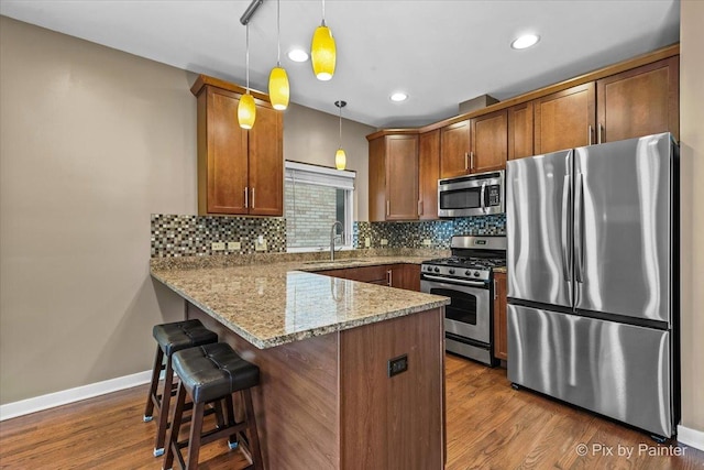 kitchen with decorative light fixtures, stainless steel appliances, a sink, a peninsula, and a kitchen bar