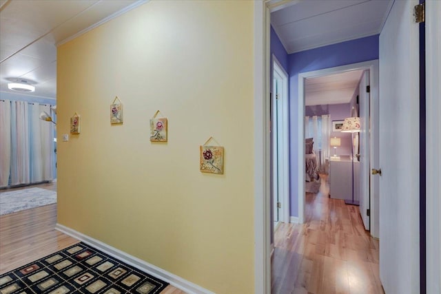 hall featuring light wood-type flooring, baseboards, and ornamental molding