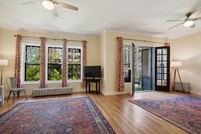 unfurnished room featuring radiator heating unit, light wood-type flooring, a ceiling fan, and baseboards