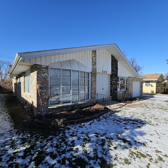 view of snow covered exterior with board and batten siding and a garage