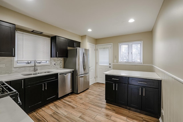 kitchen featuring appliances with stainless steel finishes, wainscoting, a sink, and dark cabinetry